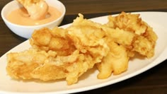 some fried food on a white plate next to a bowl of dipping sauce and a spoon