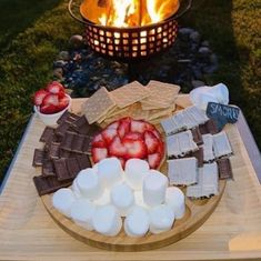 a wooden platter with marshmallows, strawberries and chocolate on it