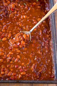 someone spooning beans into a casserole dish with red sauce on the side