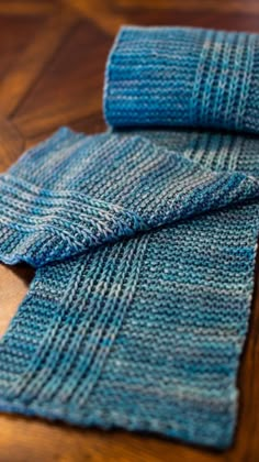 two blue knitted scarves sitting on top of a wooden table