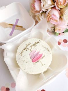 a white cake with pink icing on it sitting in a box next to flowers