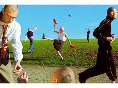 a group of people are running around in the grass and one man is wearing a tie