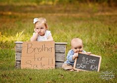 two babies sitting on top of a crate holding a sign