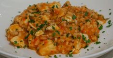 a white plate topped with shrimp and rice covered in parsley on top of a table