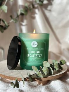 a green candle sitting on top of a wooden tray next to eucalyptus leaves and a potted plant