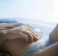 a woman laying on top of a bed next to the ocean with her hand over her stomach