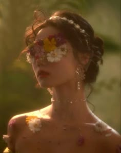 a woman with flowers on her face and hair in front of the camera, looking at something