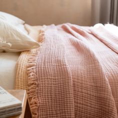 an unmade bed with a pink blanket on top of it next to a book