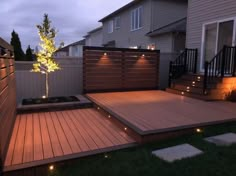 a wooden deck with lights around it and a small tree in the middle, surrounded by grass