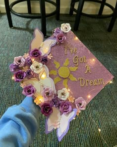 someone is holding up a purple graduation cap decorated with flowers and fairy lights that says i've got a dream