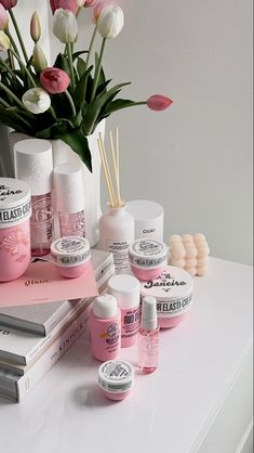 a white table topped with lots of pink and white items next to a vase filled with tulips