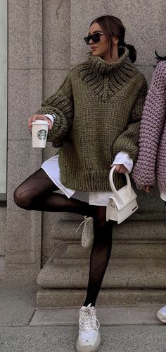 two women in sweaters and white shoes are holding coffee cups while standing next to each other