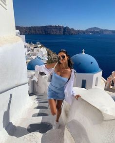 a woman in a blue dress is walking down the stairs by the water with her hands on her hips