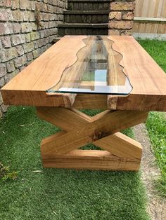 a wooden table with glass top sitting in the grass next to a brick wall and stairs