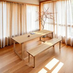 a wooden table sitting in front of a window next to a white bench with a vase on it