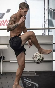 a man kicking a soccer ball on top of a hard wood floored floor in front of a window