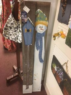 two snowmen standing next to each other in front of a wooden board with clothes hanging on it