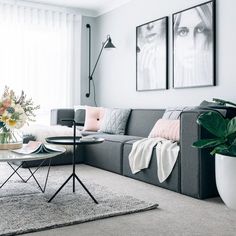 a living room with grey couches and pink pillows on the table in front of two pictures