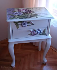 a white table with flowers painted on the top and bottom, sitting in front of a window