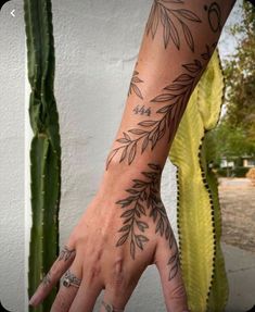 a woman's hand with tattoos on it and a cactus behind her, in front of a white wall