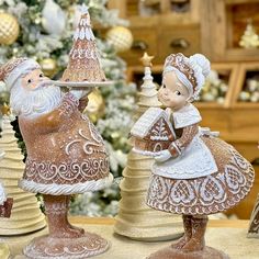 three christmas figurines are sitting on a table in front of a christmas tree