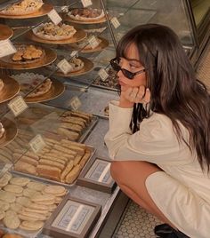 a woman sitting in front of a display case filled with donuts