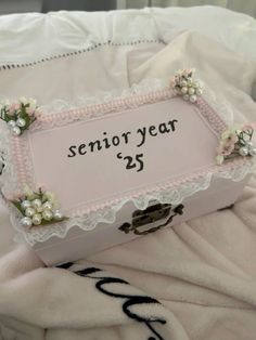 a pink and white box sitting on top of a bed covered in blankets with flowers