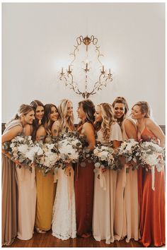 a group of women standing next to each other holding bouquets in front of a chandelier