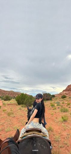 a woman riding on the back of a brown horse in an open field with red dirt