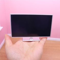 a hand holding a small computer monitor in front of a pink wall