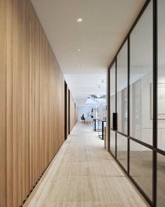 the hallway is lined with wooden slats and glass walls, along with people sitting at their desks