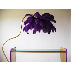 a purple plant sitting on top of a glass table next to a yellow lamp and a book