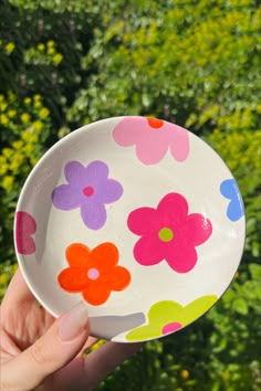 a hand holding a colorful flowered bowl with trees in the background