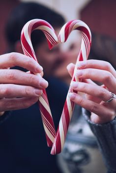 two hands holding candy canes in the shape of a heart with a man kissing behind them