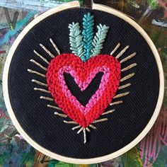 a red heart with an arrow in the center is surrounded by green and pink needles