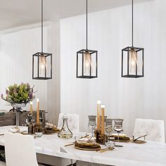 a dining room table with white chairs and lights hanging from the ceiling, along with two vases filled with flowers