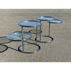 three glass tables sitting on top of cement ground next to each other with circular metal bases