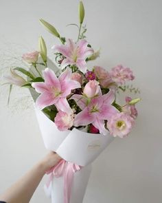 a bouquet of pink flowers in a white vase with someone's hand holding it