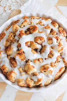 a white bowl filled with cinnamon rolls covered in icing