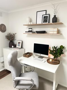 a white desk with a computer monitor and keyboard on top of it next to a plant