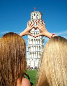 two girls standing in front of a tower with their hands up to the sky above them