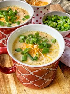 three bowls filled with soup on top of a wooden table next to green onions and cheese