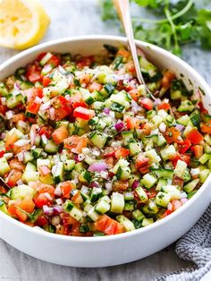 a white bowl filled with cucumber and tomato salad next to a lemon wedge