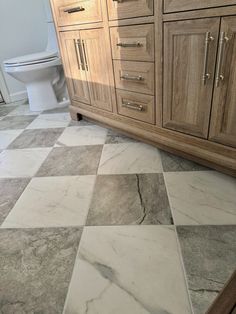 a white toilet sitting next to a wooden cabinet on top of a tiled floor in a bathroom