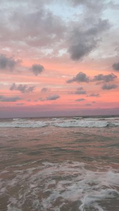 the sky is pink and cloudy over the ocean at sunset with waves coming in to shore