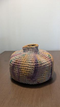 a crocheted basket sitting on top of a wooden table next to a white wall