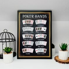 a black and gold framed poster with playing cards on it next to potted plants