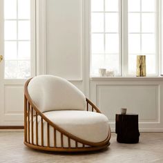 a white chair sitting in front of a window next to a wooden table and vase