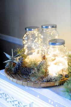 two mason jars filled with lights sitting on top of a wooden tray covered in snow