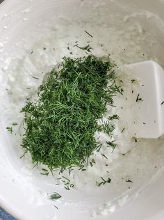 a white bowl filled with sour cream and chopped green sprigs on top of it